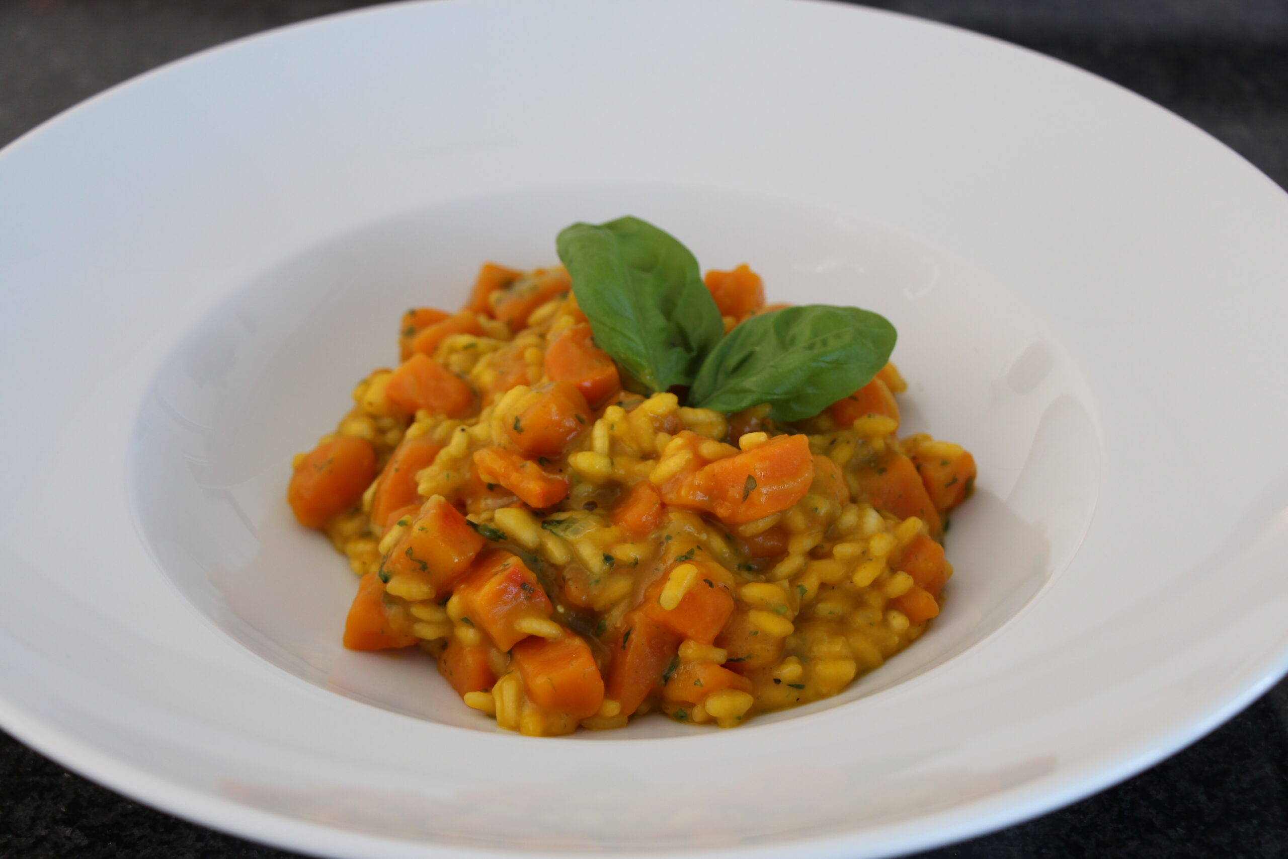 Kürbisrisotto mit Kürbiswürfeln und Basilikum auf einem weißen Teller