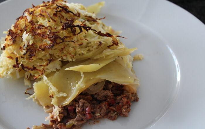 Wirsingauflauf mit Kartoffelscheiben, Tatar und Kochkäse auf einem weißen Teller