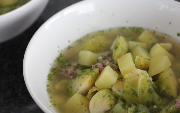 Rosenkohleintopf mit Kartoffeln und kleinen Tatarbällchen auf einem weißen Teller