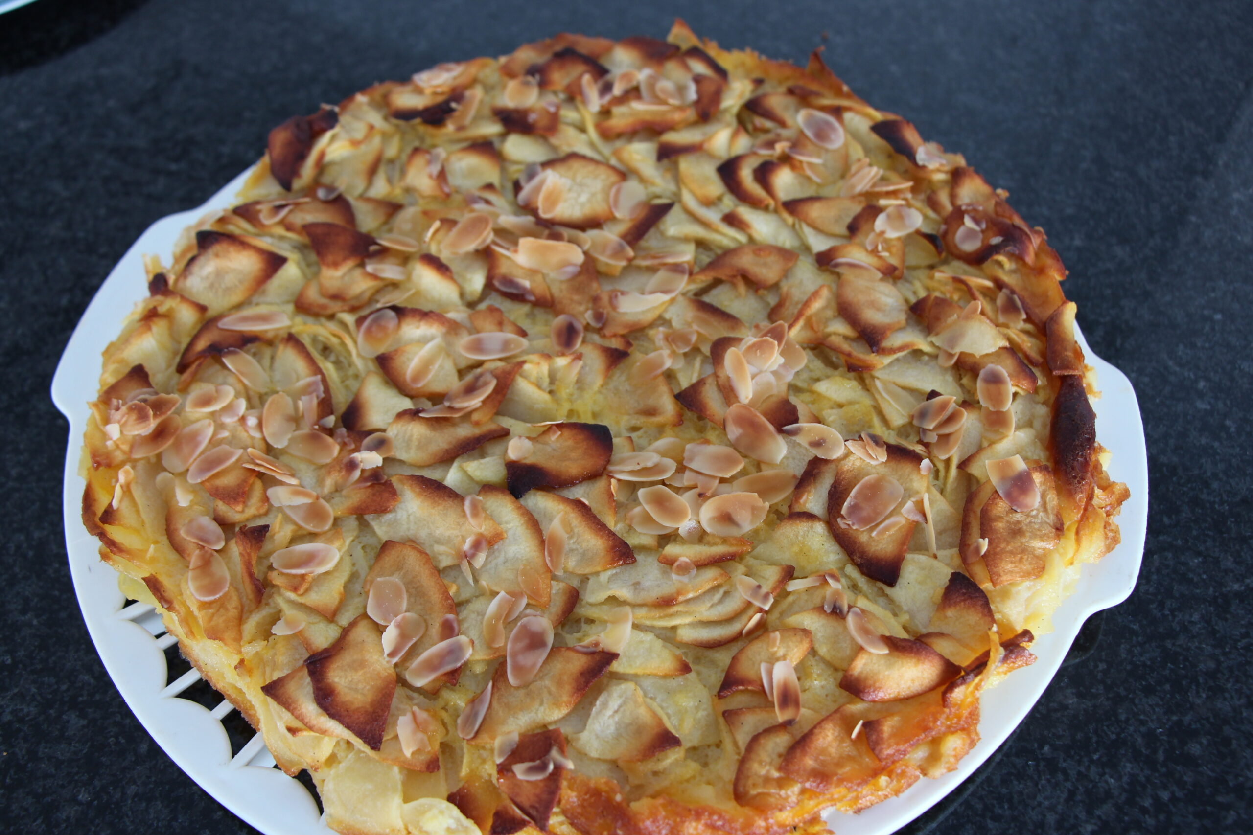 Torta di Mele mit dünnen Apfelscheiben und zusätzlichen Mandelblättchen auf einer Kuchenplatte