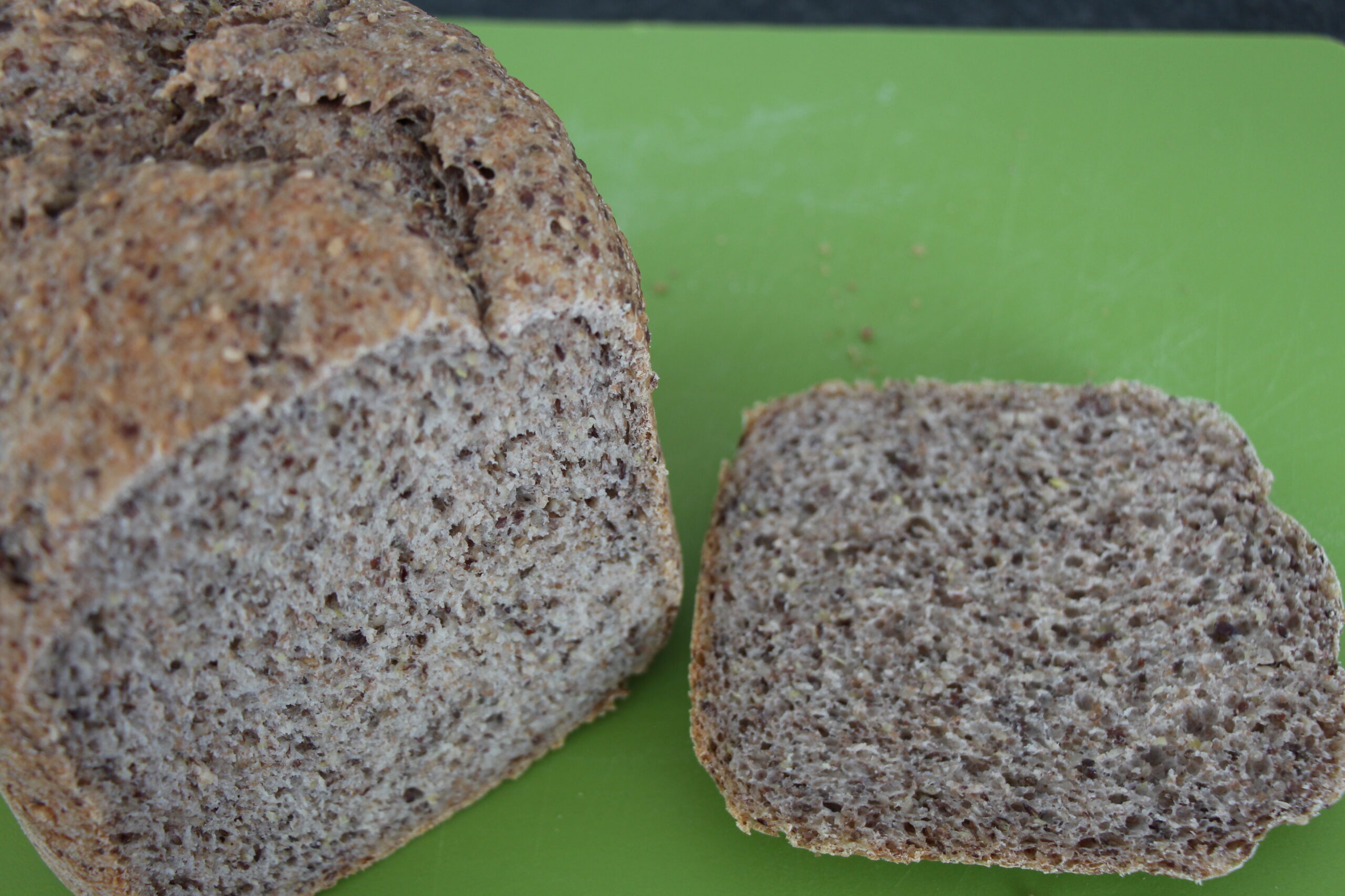 Angeschnittenes Chia-Brot mit Leinsamen und Sesam auf einem grünen Schneidebrett